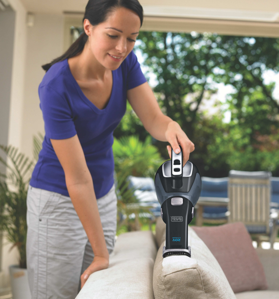 Woman using a Dustbuster Cordless Hand Vacuum to vacuum the top of a sofa cushion.