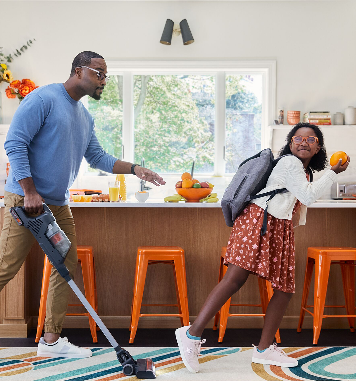 dad playfully chasing daughter with BLACK+DECKER Powerseries+ stick vacuum in kitchen