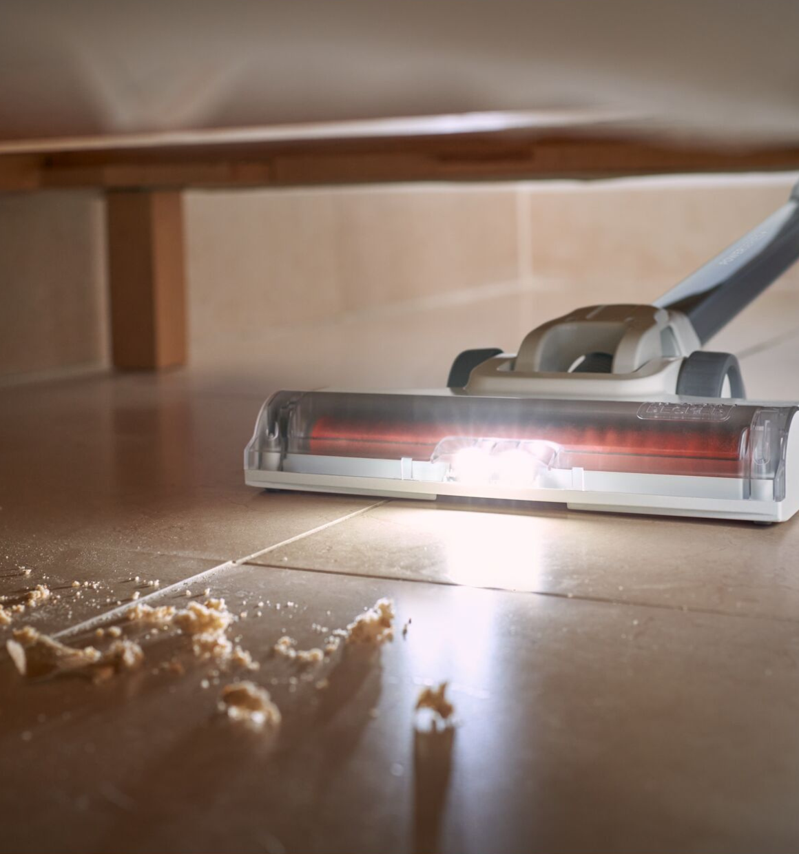 Powerseries plus 20 volts MAX cordless stick vacuum kit with Led floor light being used to clean up a mess on floor tiles underneath furniture.