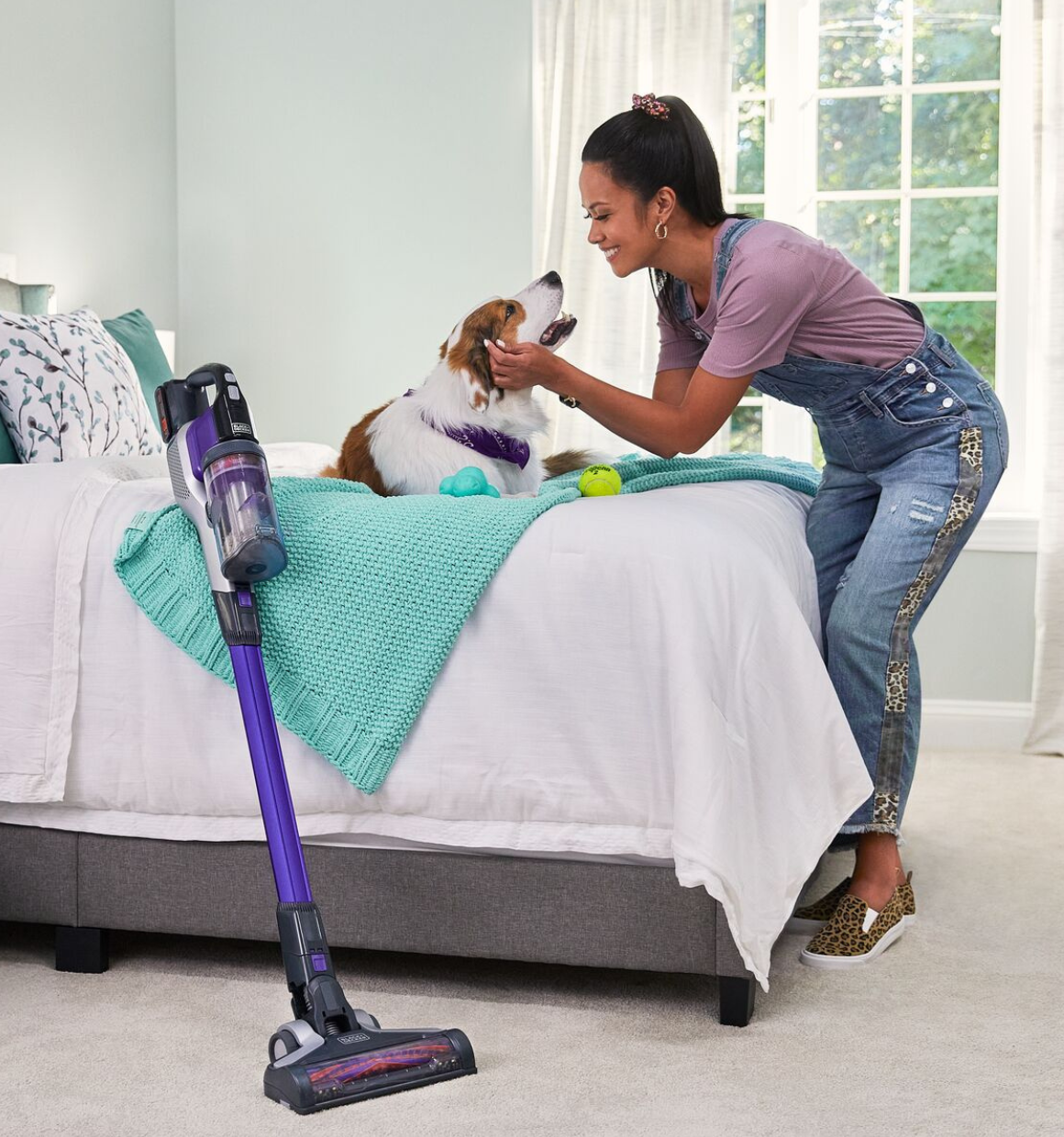 woman petting her dog while taking a break from vacuuming bedroom carpet with BLACK+DECKER PowerseriesExtreme pet stick vacuum