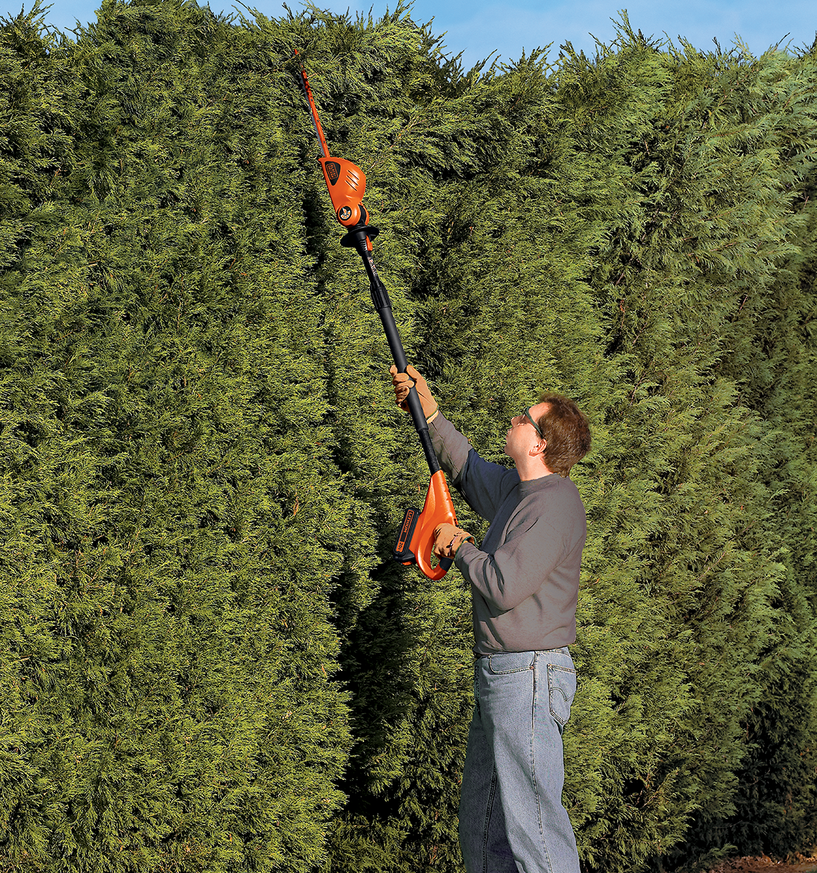 MAX Lithium Pole Hedge Trimmer being used by person to trim long heighted shrubs outdoors.