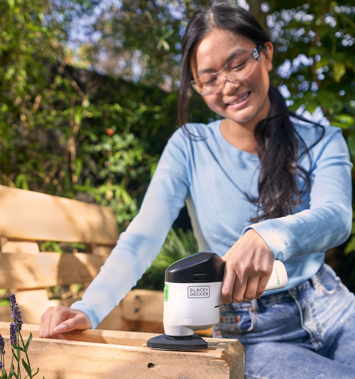 Woman using a Reviva 12V Sander on the arm of an outdoor bench.
