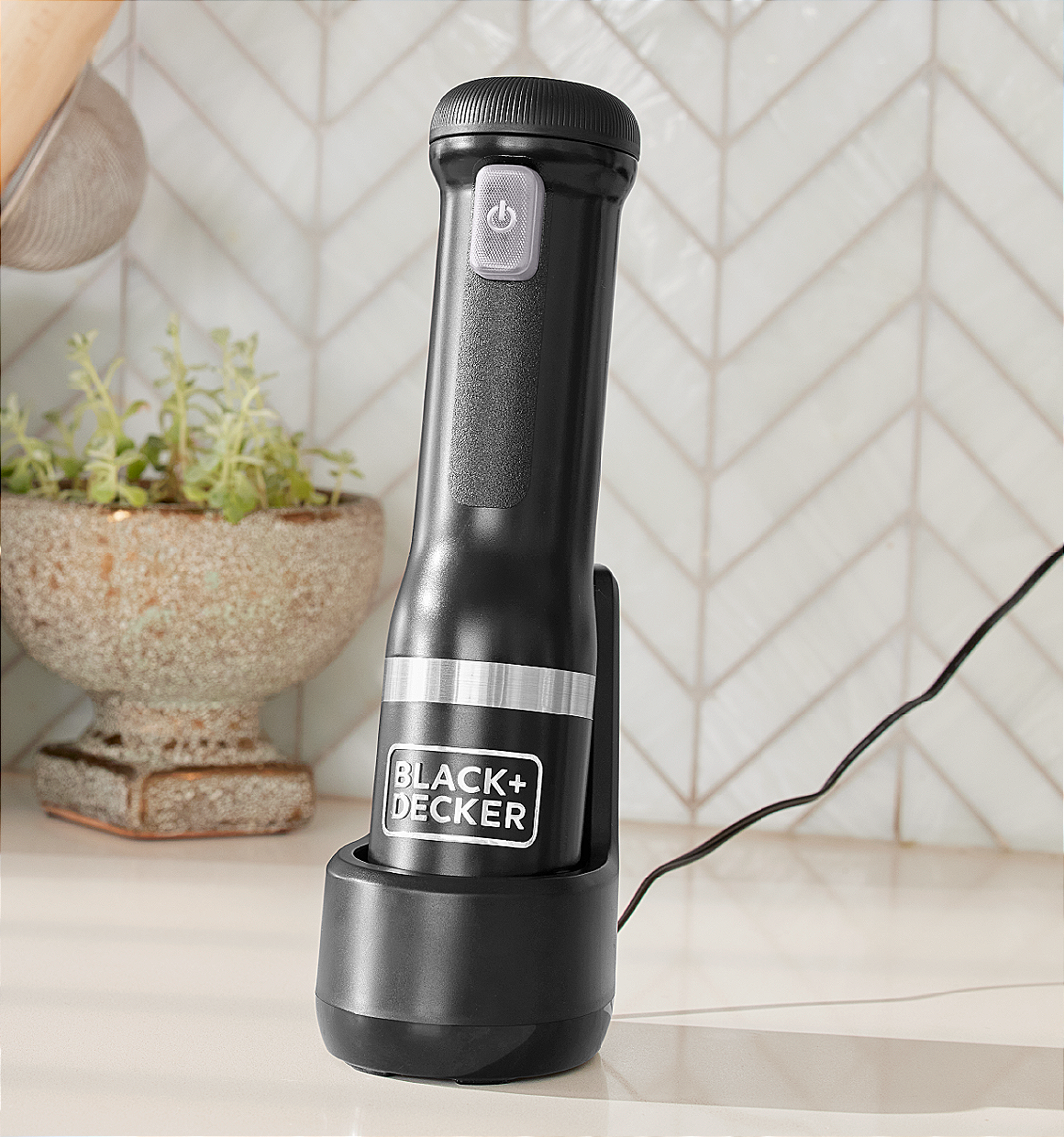 3/4 view of the black, BLACK+DECKER kitchen wand power unit charging in the charging dock on a kitchen countertop