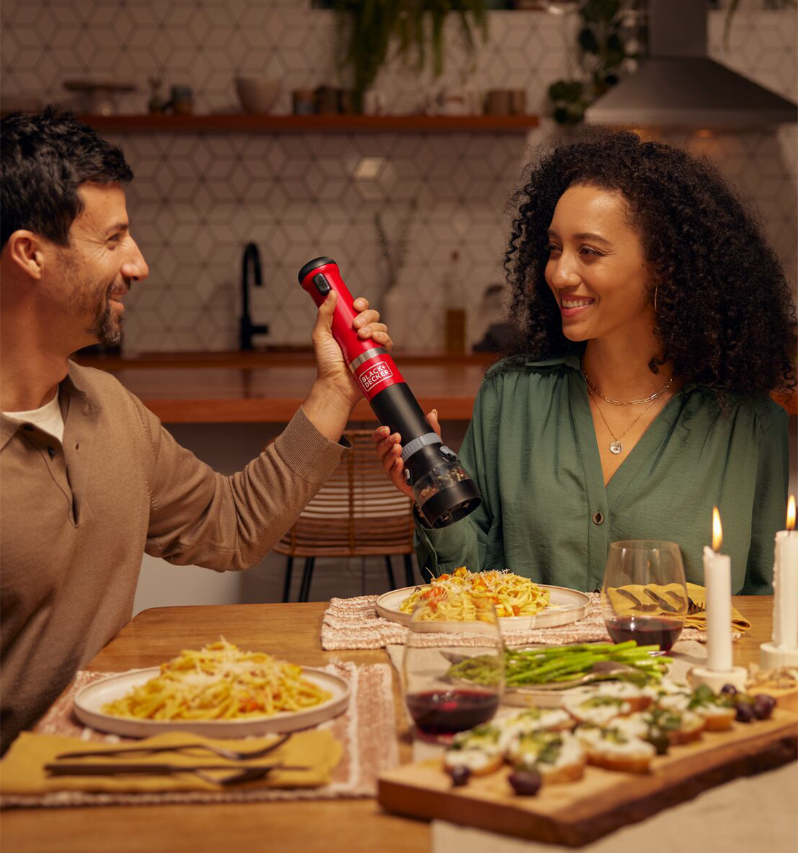 Talent using the red, BLACK+DECKER kitchen wand spice grinder at a table over dinner.