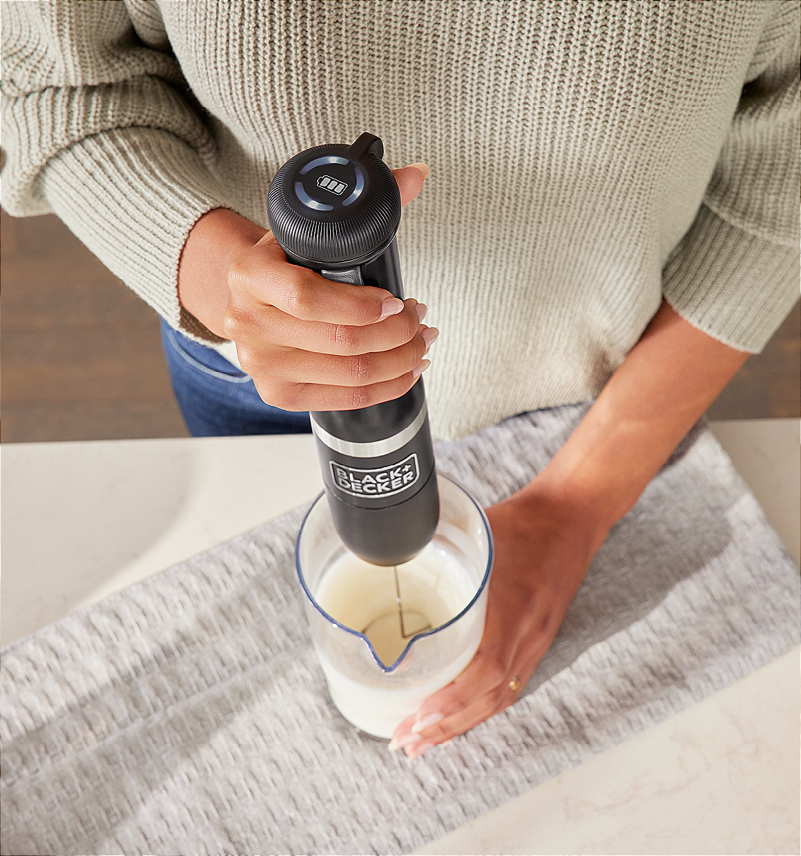 Talent using the black, BLACK+DECKER kitchen wand milk frother to froth milk in mixing cup