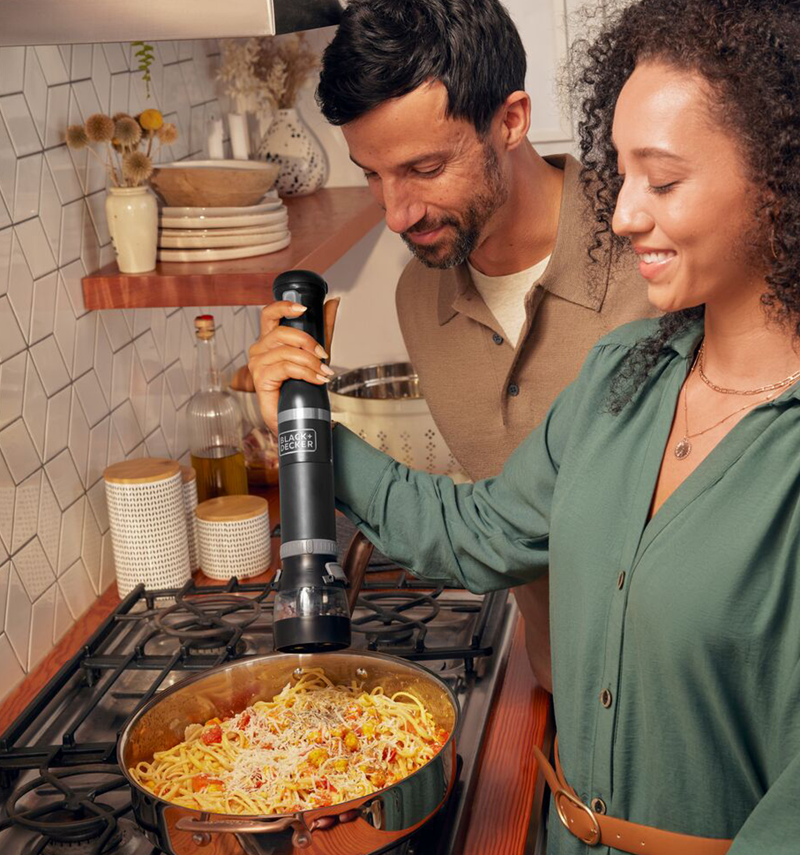 Talent using the grey, BLACK+DECKER kitchen wand spice grinder to add spices to a pasta entrée
