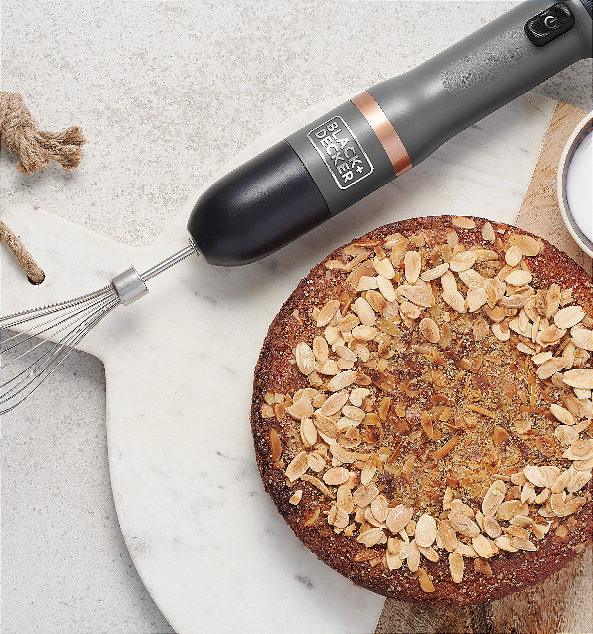 Grey, BLACK+DECKER kitchen wand whisk lying on the countertop next to a pie