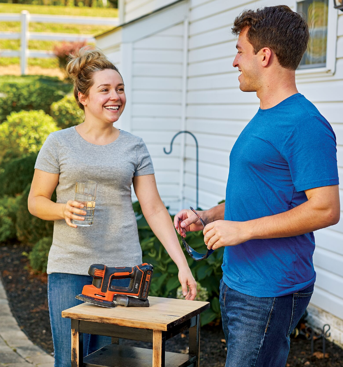 Two adults taking a break from a project while a 20 volt max mouse cordless sander waits on a partially sanded table