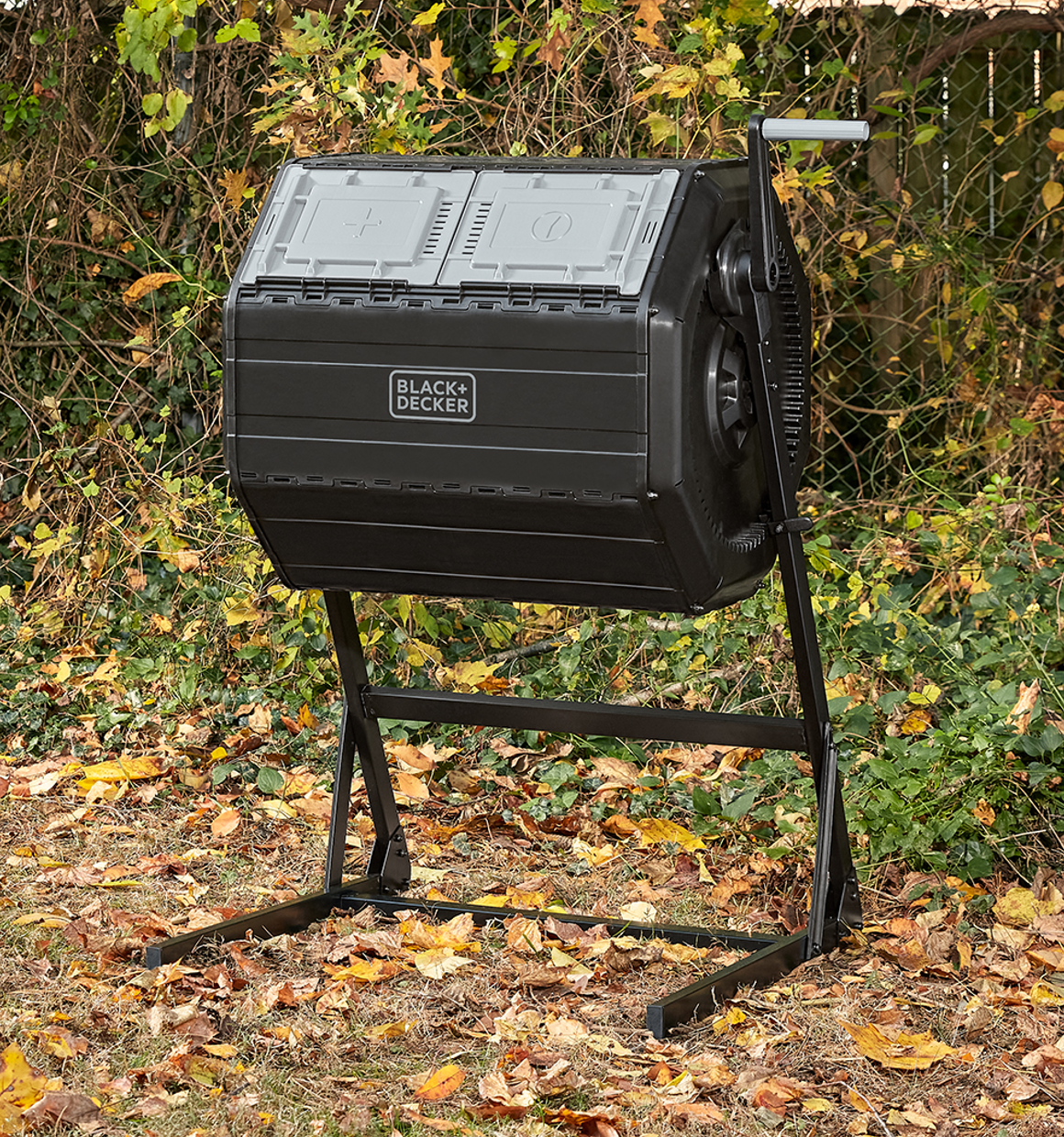 The BLACK+DECKER 40 Gallon Dual Chamber Tumbler Composter sitting in open space in a yard with trees in the background
