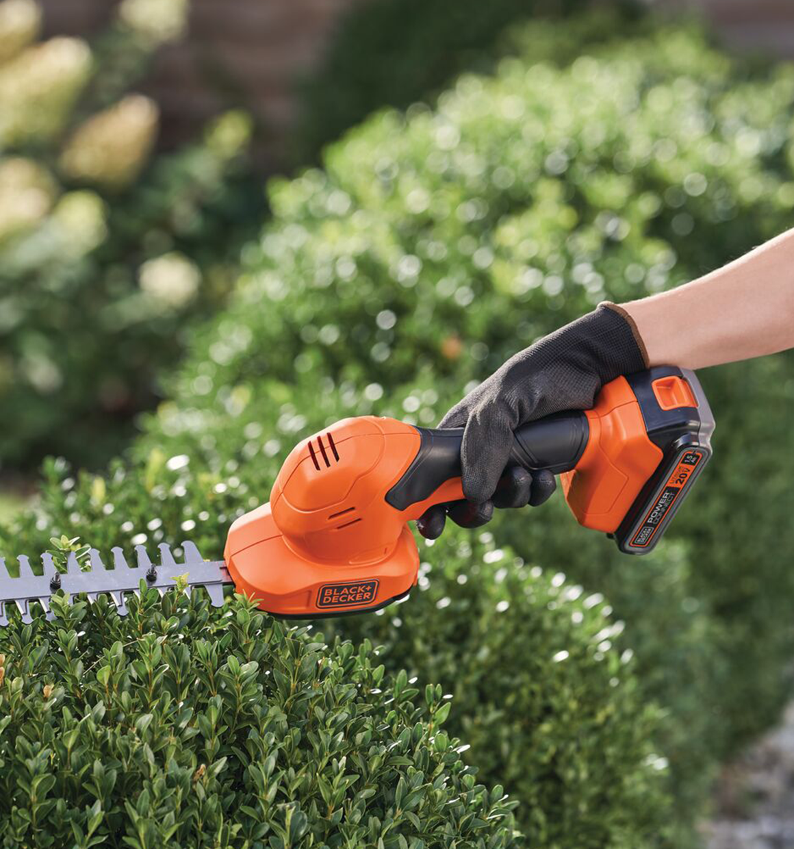 Black and Decker cordless shear shrubber being used to trim a hedge.