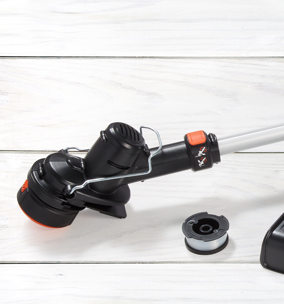 Close up of trimmer head of a lithium string trimmer battery and charger not included with spool next to it.