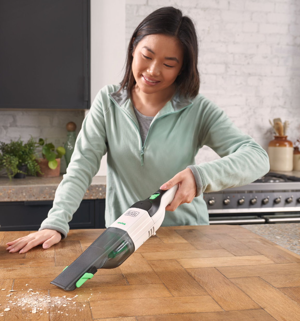 Smiling woman cleaning countertop spill with a 8V Reviva Hand Vacuum.