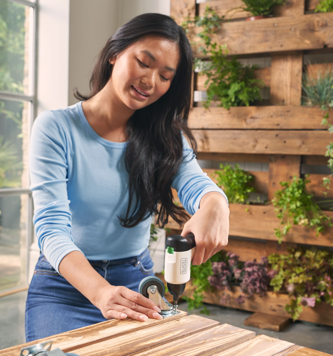Woman using a Reviva 4V Screwdriver to secure casters to the bottom of wooden bins.