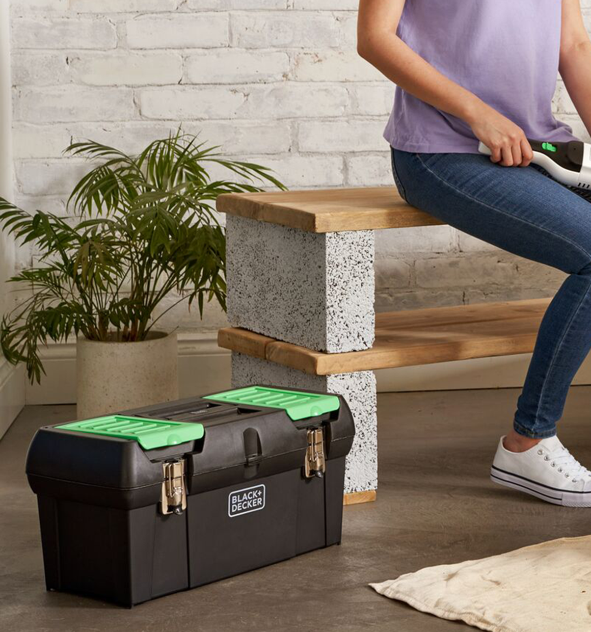 BLACK+DECKER reviva toolbox on the floor next to a woman on a bench.