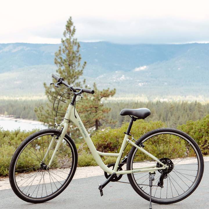 A light olive green bicycle rests on a path, surrounded by lush greenery and mountains under a cloudy sky.