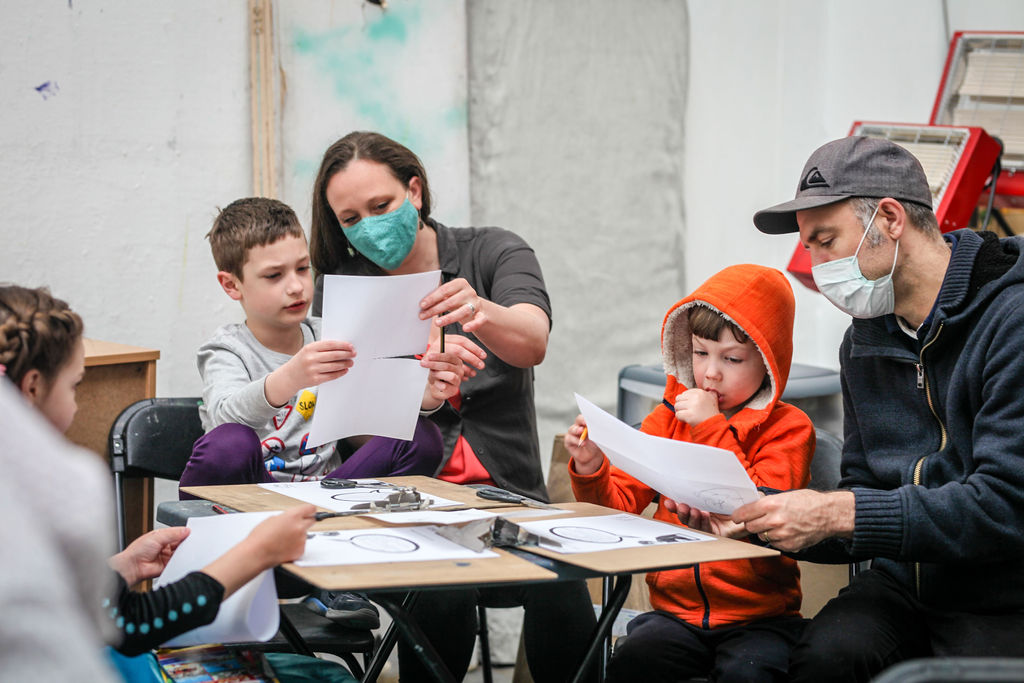 An image of a woman and a man with three children sat behind a table looking at their drawings 