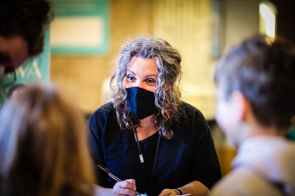 An image of a woman with a mask on with the back of two children's heads out of focus on the left and right 