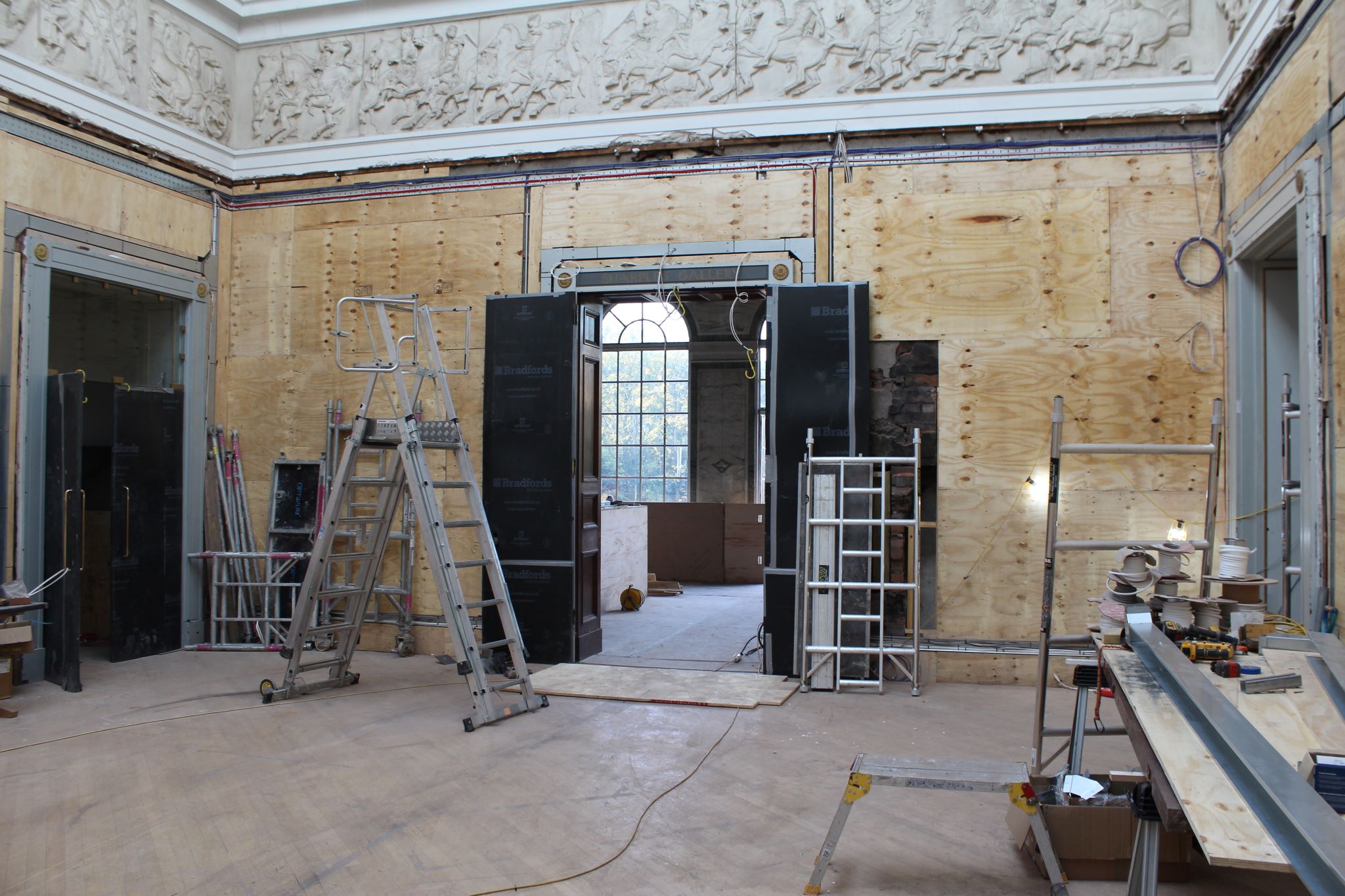 Inside the RWA gallery space with ladder and building materials, a bright window provides light at the far side 