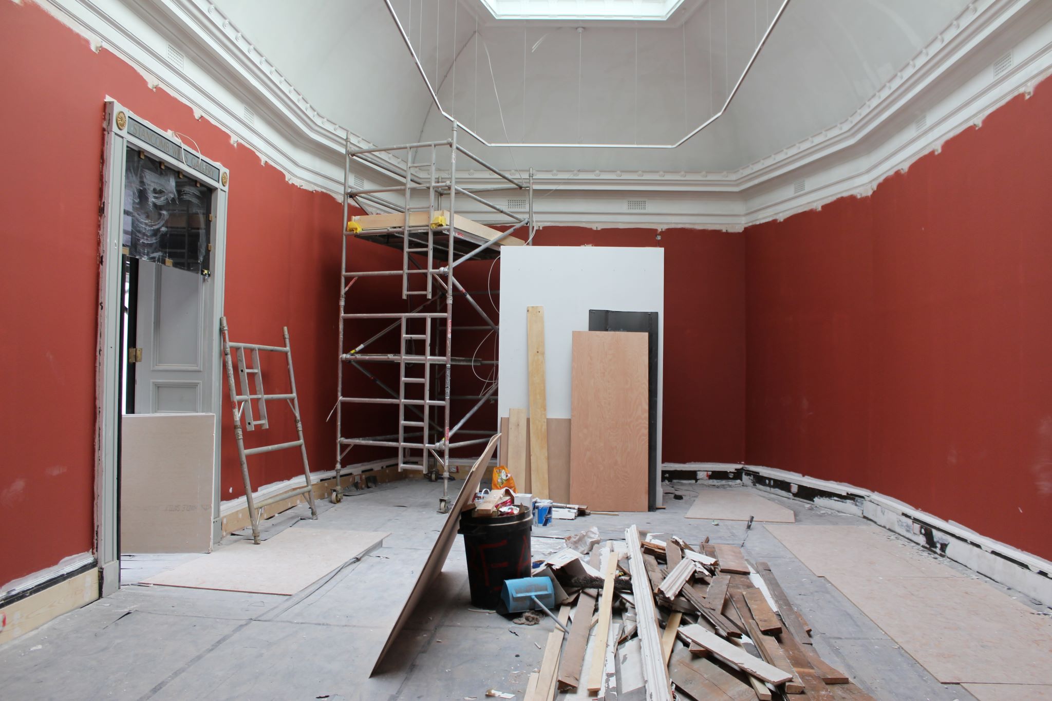 A gallery space with building materials in the centre and red painted walls 