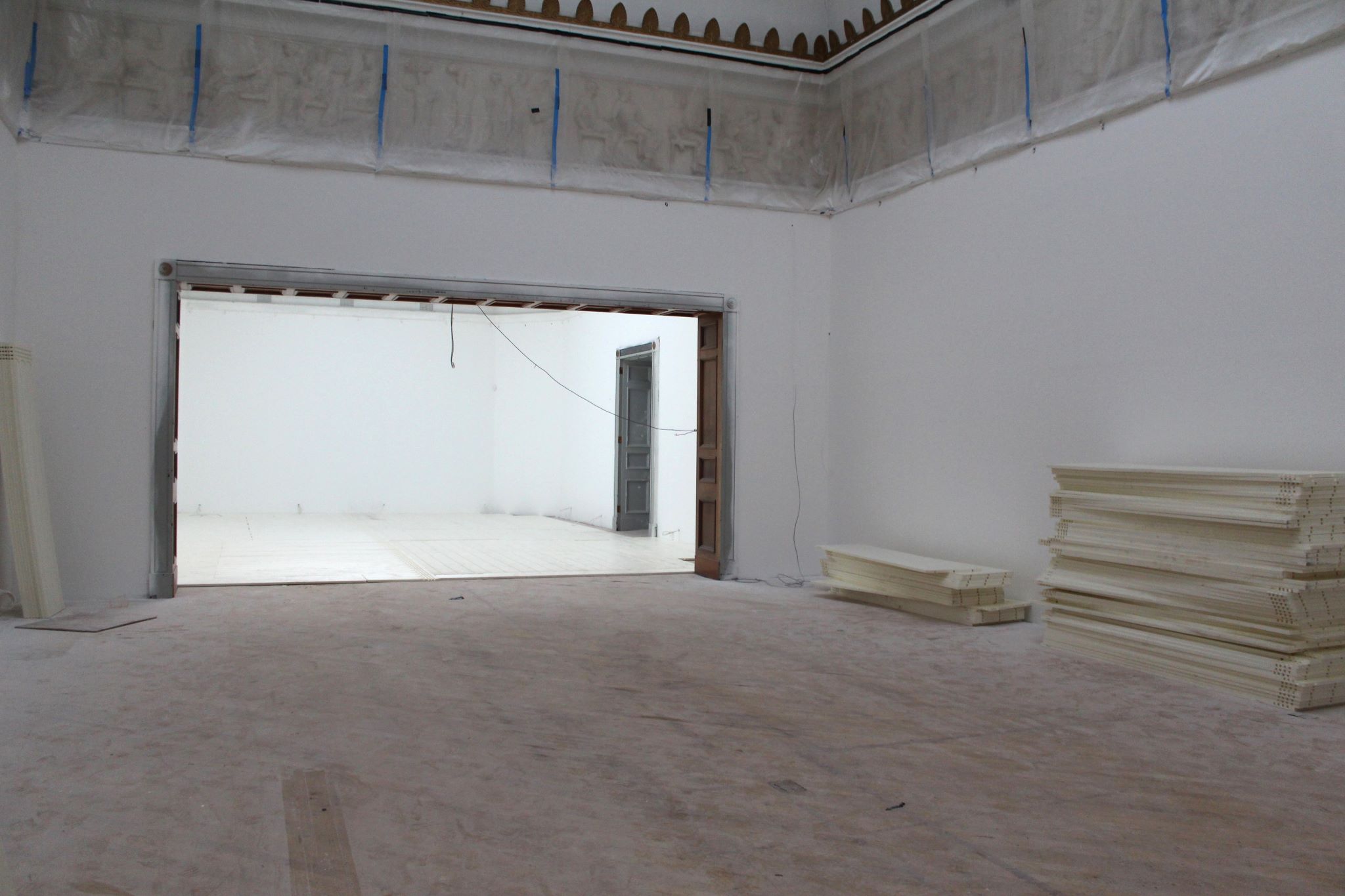 Two large gallery spaces with floorboards removed and piles of flooring to the side of the space 
