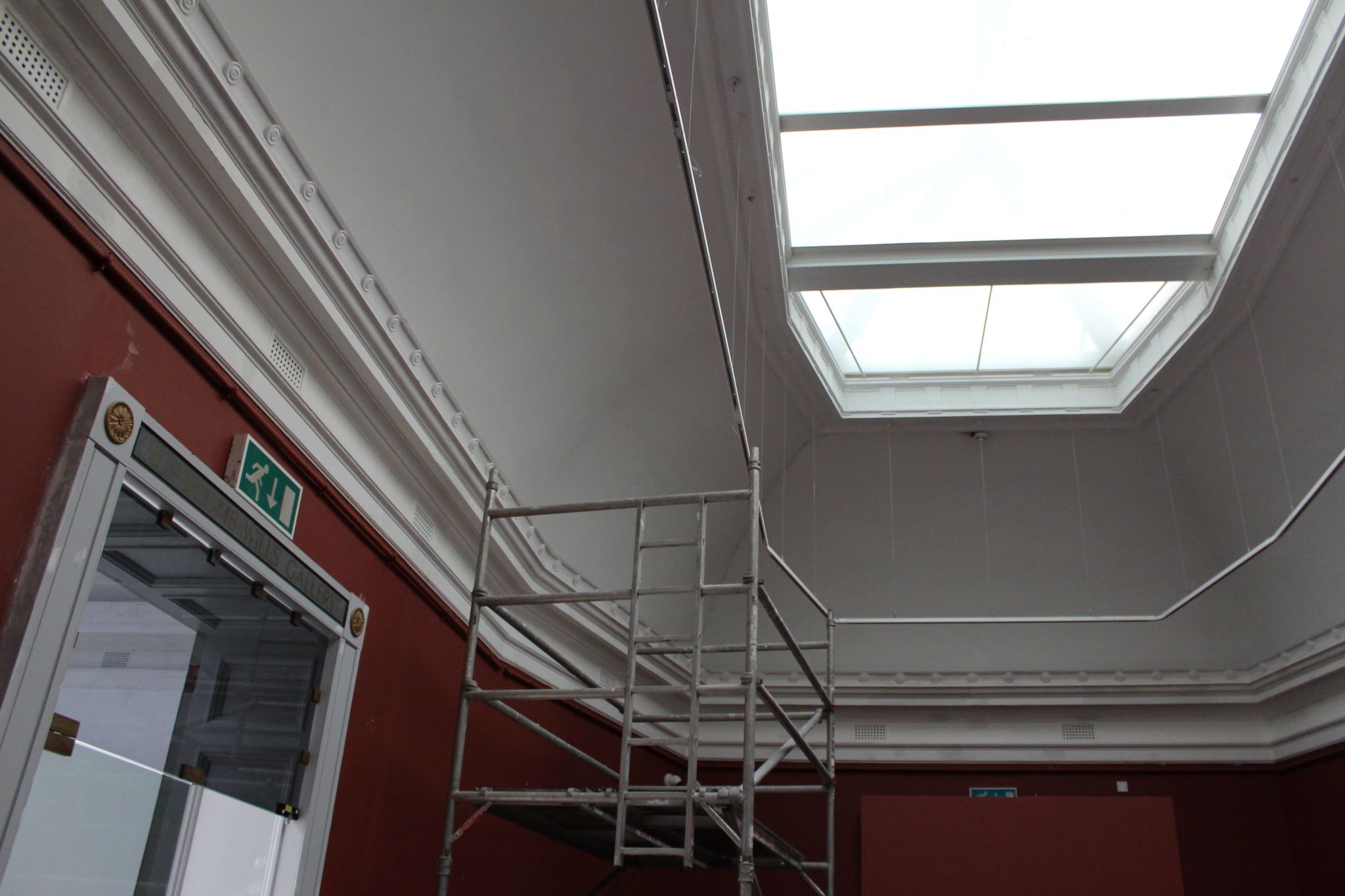 A large skylight surrounded by white ceiling and red painted walls, scaffolding is central in the room 