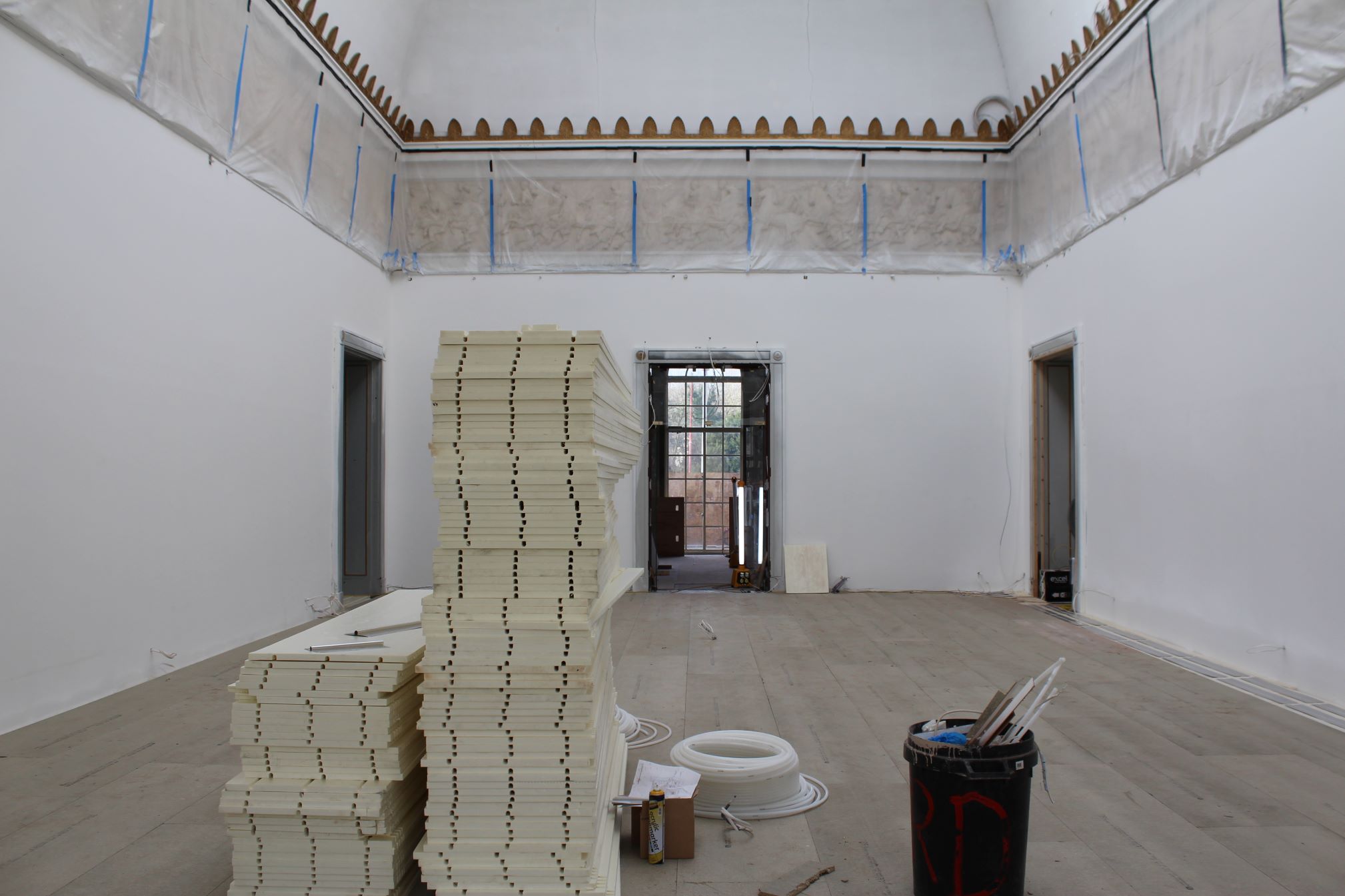 A large gallery space with piles of floorboards and tools in the centre of the room 