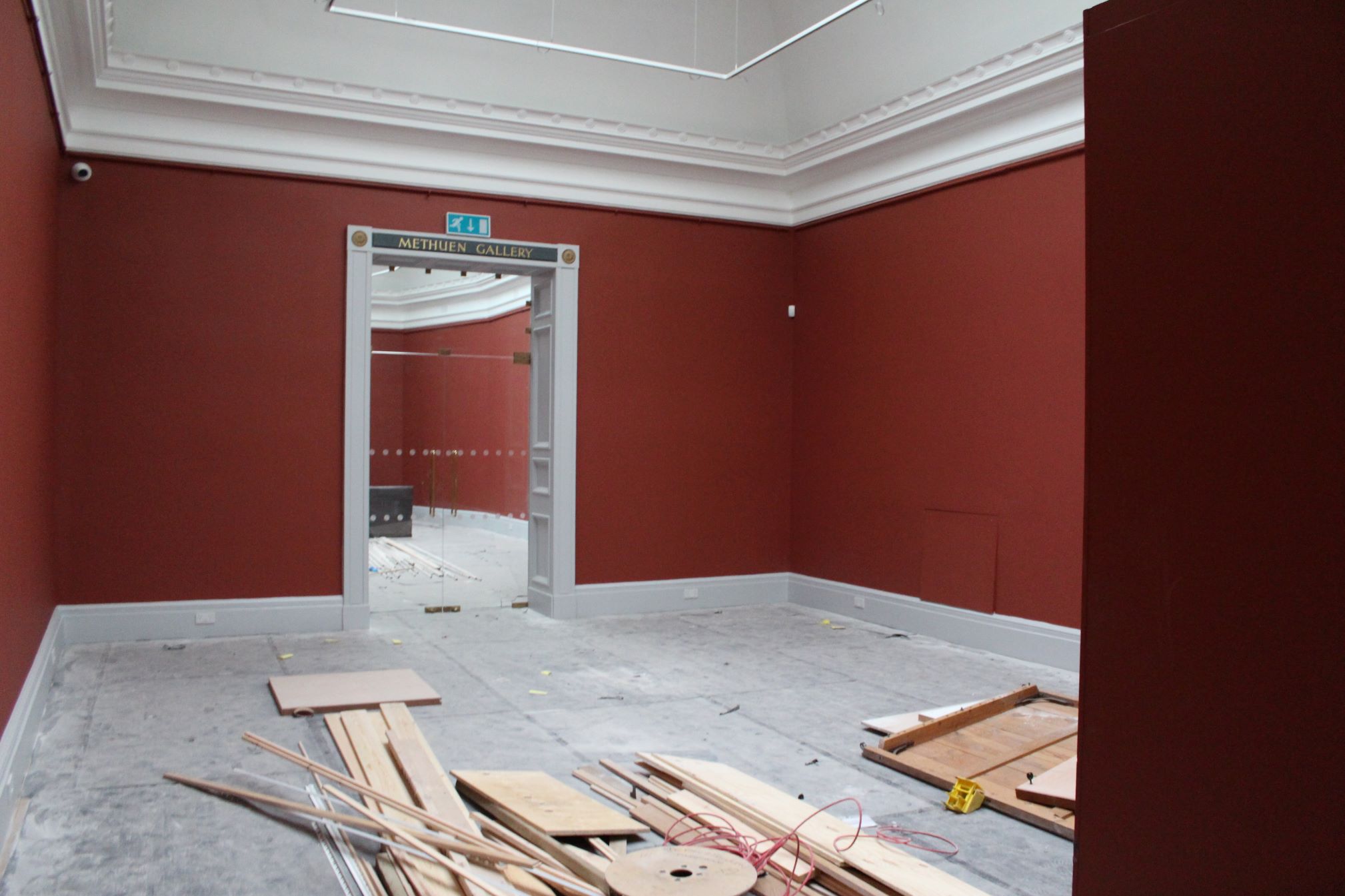 A gallery space with walls painted dark red and floorboards in the centre of the space 