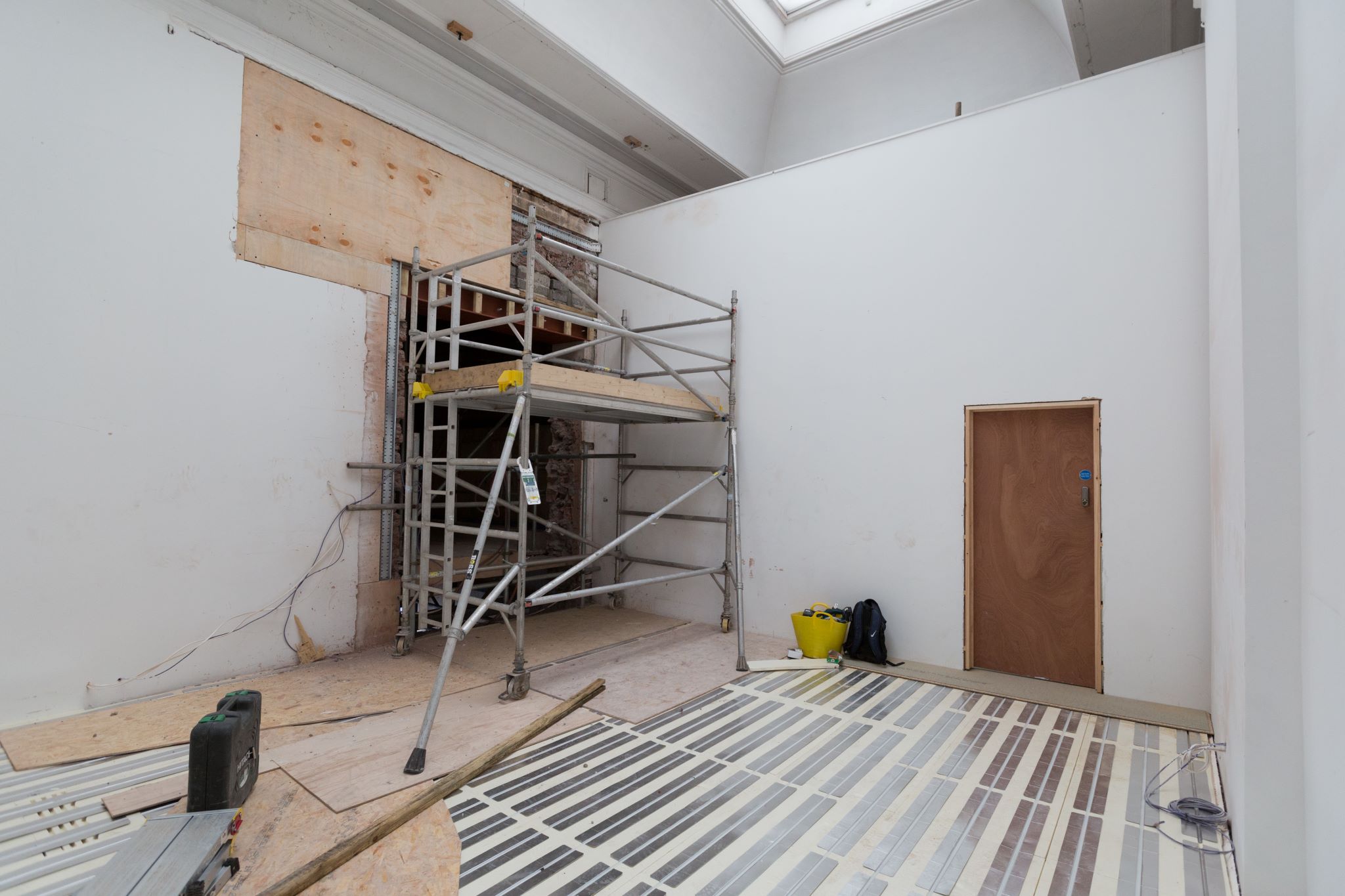 A room with flooring being installed and scaffolding at the far side 