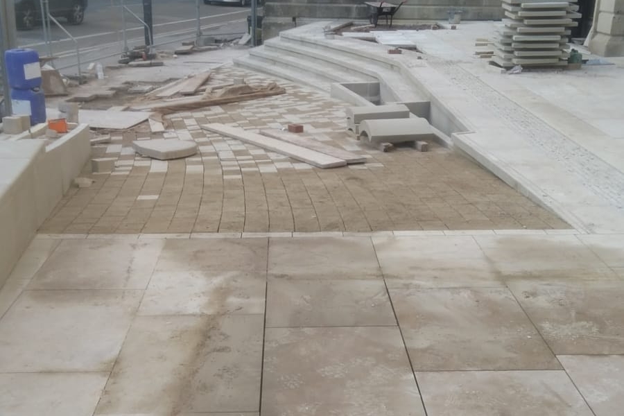 An outdoor space with paving stone fitted and piles of stone in the background 