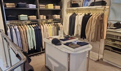 N.Peal Covent Garden store interior with racks of neatly hung jackets and shirts in soft neutral and pastel tones, shelves of folded knitwear, and a central display table with accessories