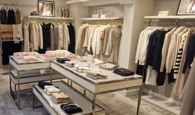 Covent Garden store interior with racks of neutral-toned clothing, folded garments displayed on layered tables, and a large mirror reflecting the space