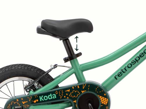 Green Koda 12 inch kid's bike showing adjustable seat height with arrows, black saddle, and decorated chain guard.