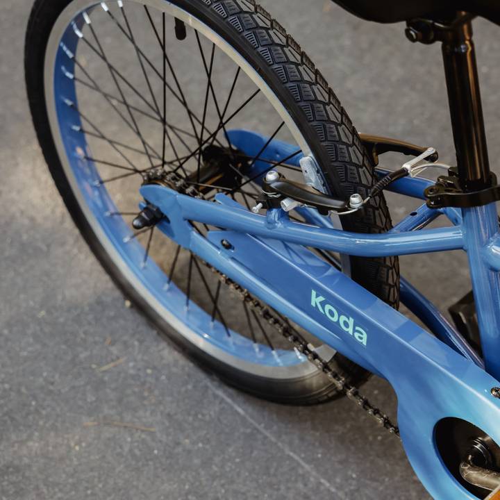 Detailed view of a blue Koda 20" Kids' Bike's chain guard and rear wheel, showcasing a black seat.