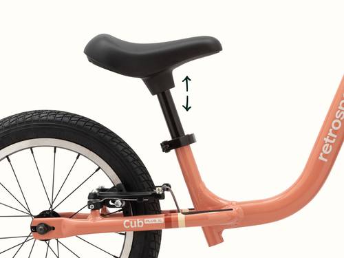 Close-up of Kids' Cub Plus XL Balance Bike rose-colored bicycle's seat with an adjustable height indicator.