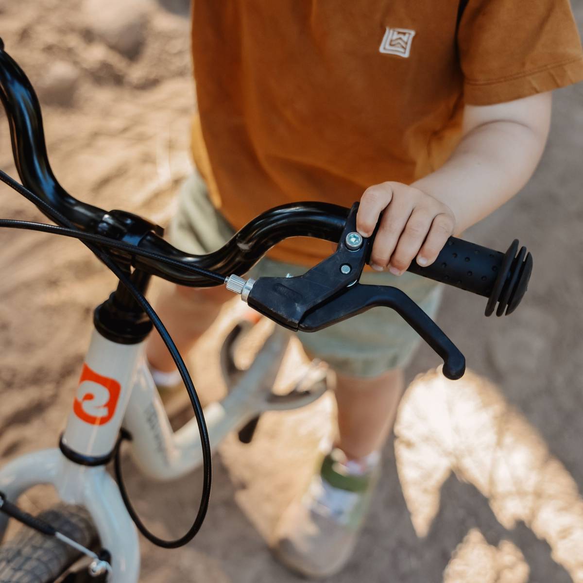 A close-up of a child holding the Cub Plus XL 14" Kids' Balance Bike's handlebars, focusing on the hand brake.