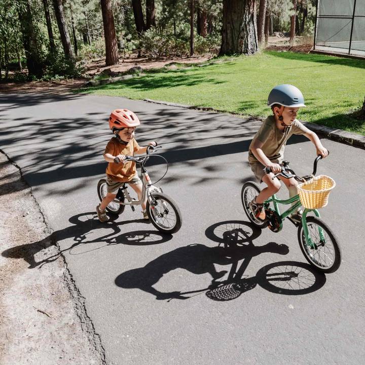 Two children riding bicycles side by side on a smooth, paved road under a clear blue sky.