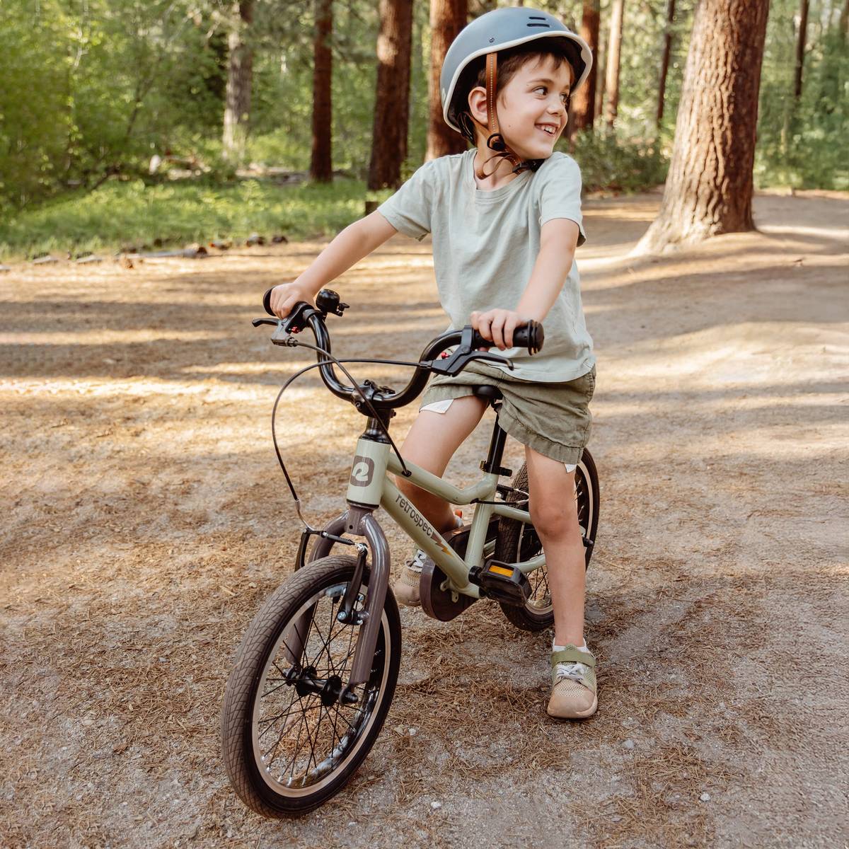 A Koda Plus 16" bike in soft green, resting against a log in a woodland setting, showcasing its sleek design and sturdy frame.