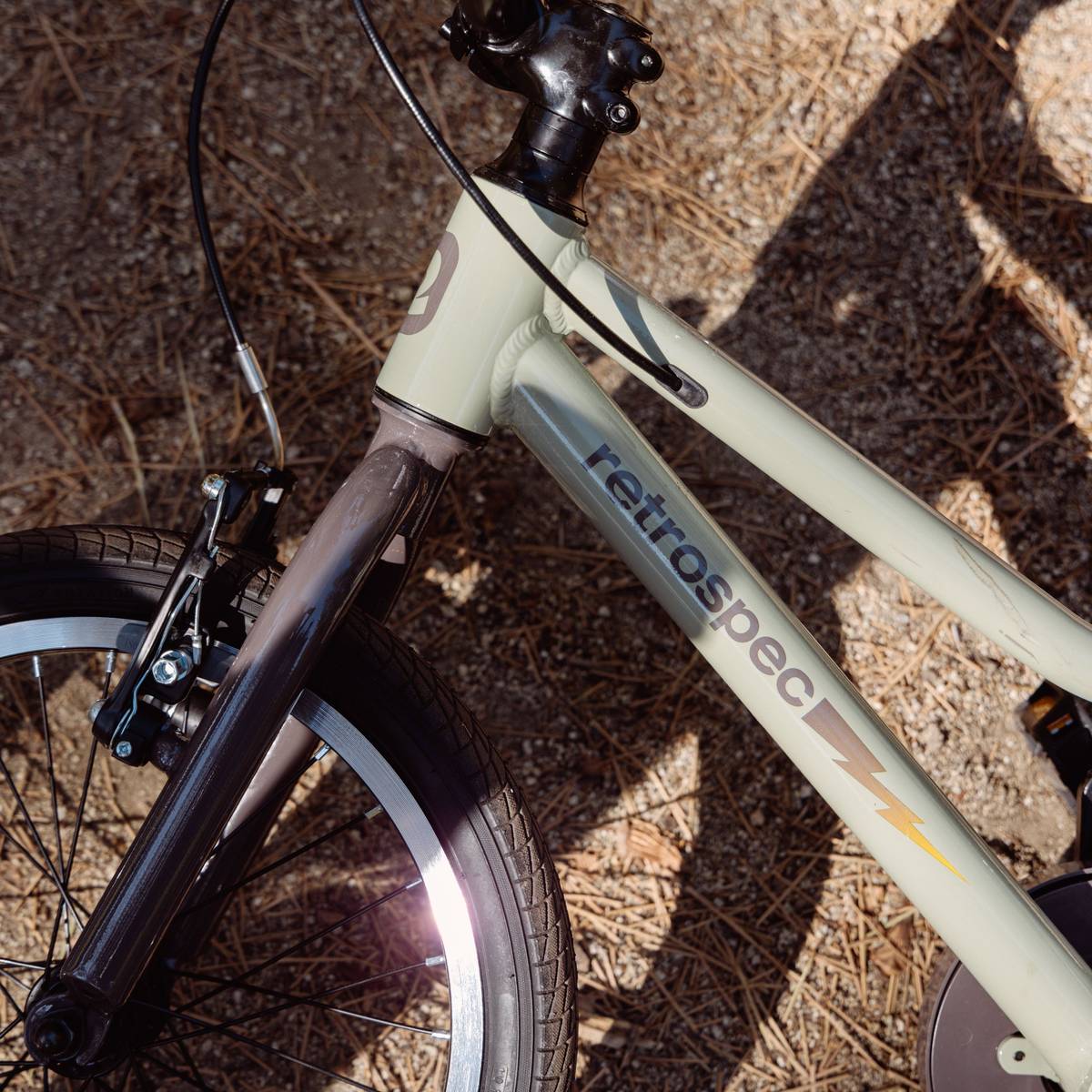Close-up of a Koda Plus 16" Kids Bike frame, showcasing its pale green color, black handlebars, and sturdy wheel against a gravel background.