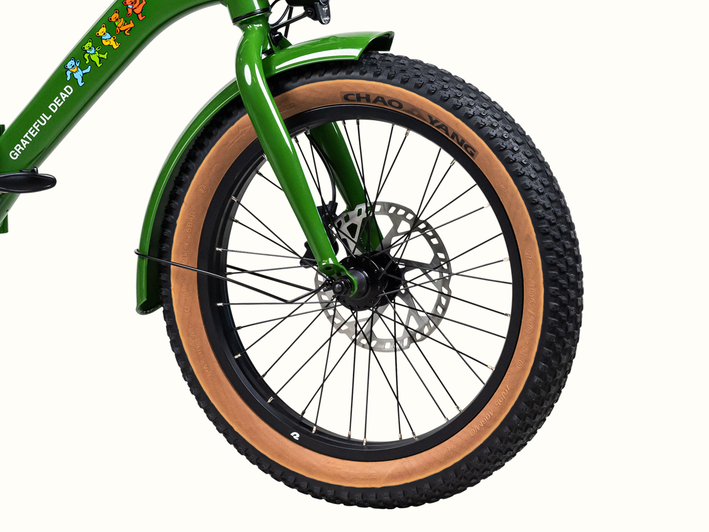 Close-up of a green bicycle front wheel featuring a disc brake and distinctive brown rubber tire, and the frame adorned with colorful Grateful Dead Dancing Bears.