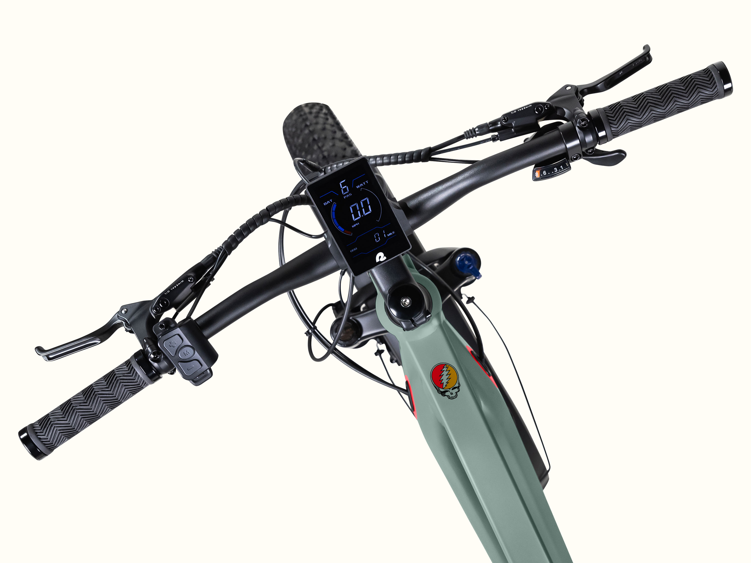 Close-up view of the green Grateful Dead Koa Rev+ 2 Fat Tire Electric Bike's handlebars featuring a digital display, grips, and brake levers, with the iconic Grateful Dead skull also known as 