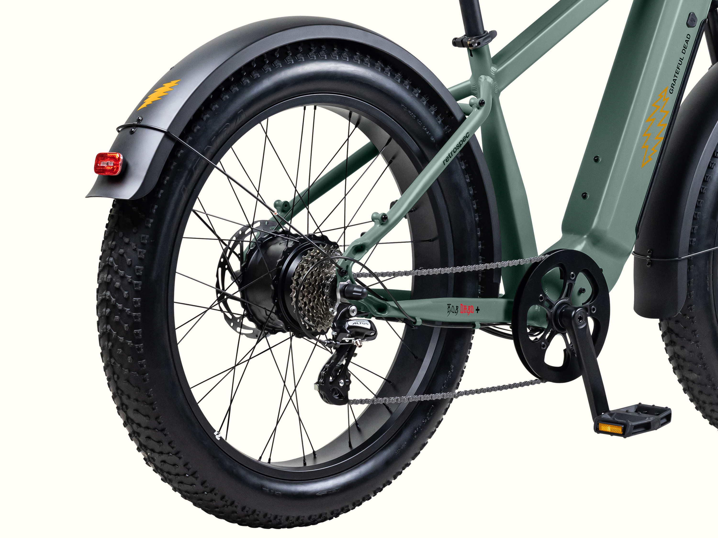 Close-up of the Grateful Dead Koa Rev+ Electric Bike's rear, showcasing fat tires, a robust chain, and a fender with a red reflector and yellow Grateful Dead lightening bolt designs.