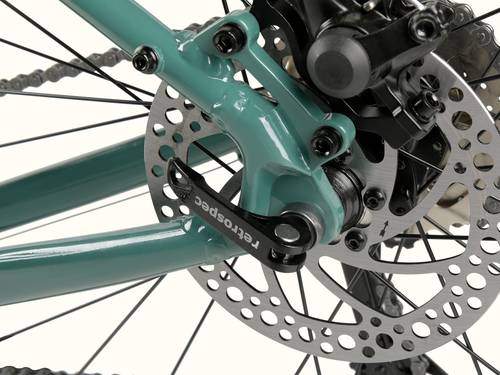 Close-up of a Grateful Dead Amok 8 Speed Gravel Adventure Bicycle rear wheel hub, featuring a green frame, disc brake, and visible chain links.