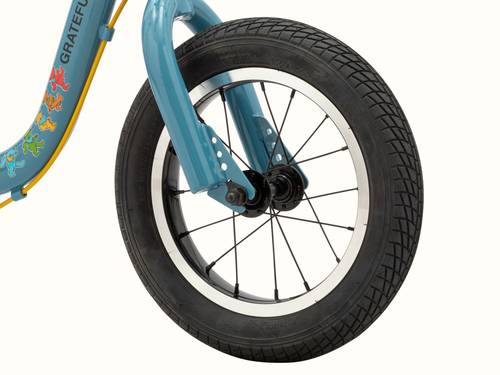 Close-up of the blue Grateful Dead Cub Plus 12" Balance Bike's front wheel featuring the "Dancing Bears" graphic on the frame and a sturdy tire with visible tread patterns.