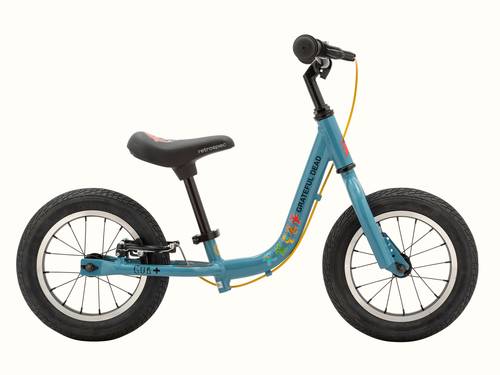 A profile view of the blue Grateful Dead Limited Edition Cub Plus Balance Bike with a black seat and colorful Grateful Dead designs including "Steal your face" and "Dancing Bears" while featuring two wheels and a sleek frame for toddlers.