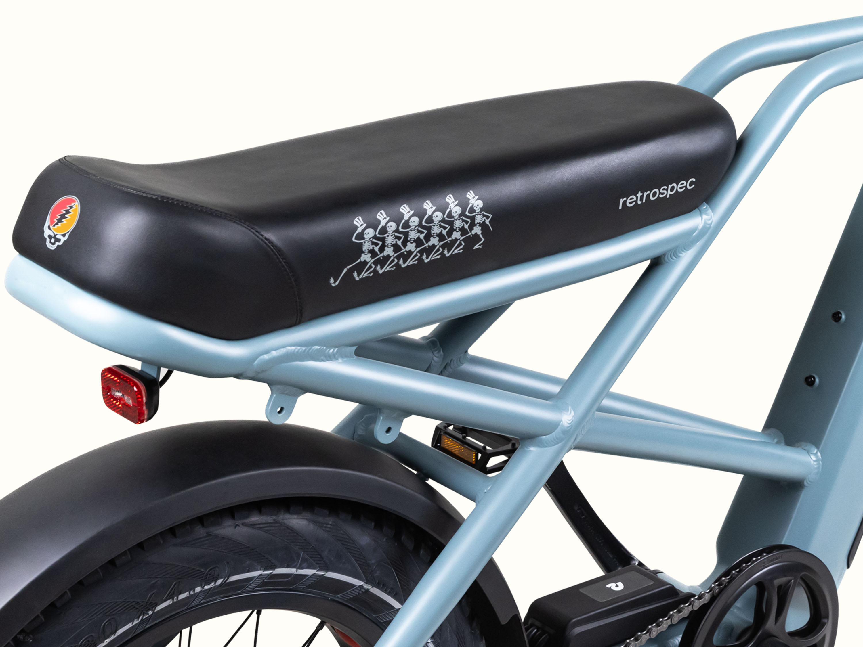 A close up of the stylish blue Grateful Dead Valen Rev+ Electric Fat Tire Bike's saddle featuring iconic Grateful Dead Dancing Skeletons and Grateful Dead Skull or 
