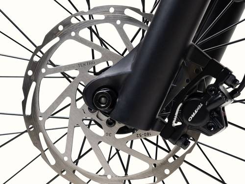 Close-up of a Tektro disc brake rotor, showcasing intricate design and mounting on a bicycle's front wheel hub and spokes.