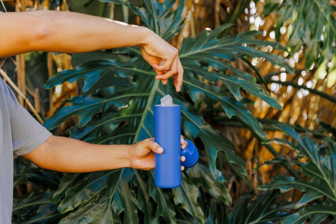 Person's arms and hands showing dropping ice into spout bottle outside.