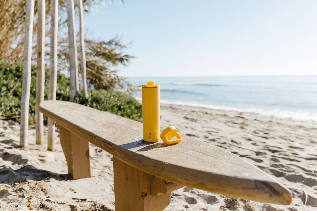 Solar Yellow spout bottle with ring lid off showing spout top on a bench with beautiful ocean in the background.