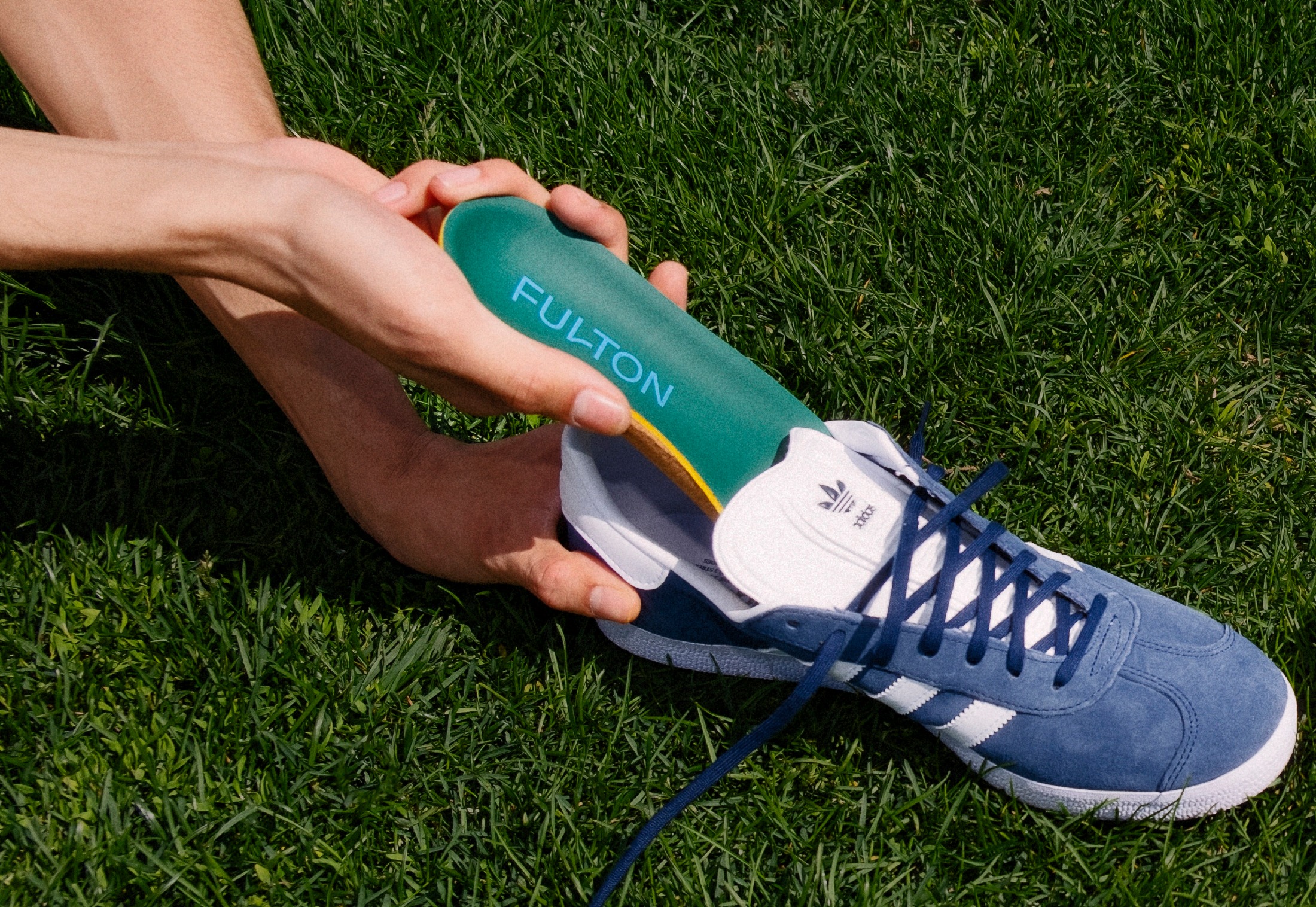 Hands holding a pair of shoes and one Fulton insert on the ground.