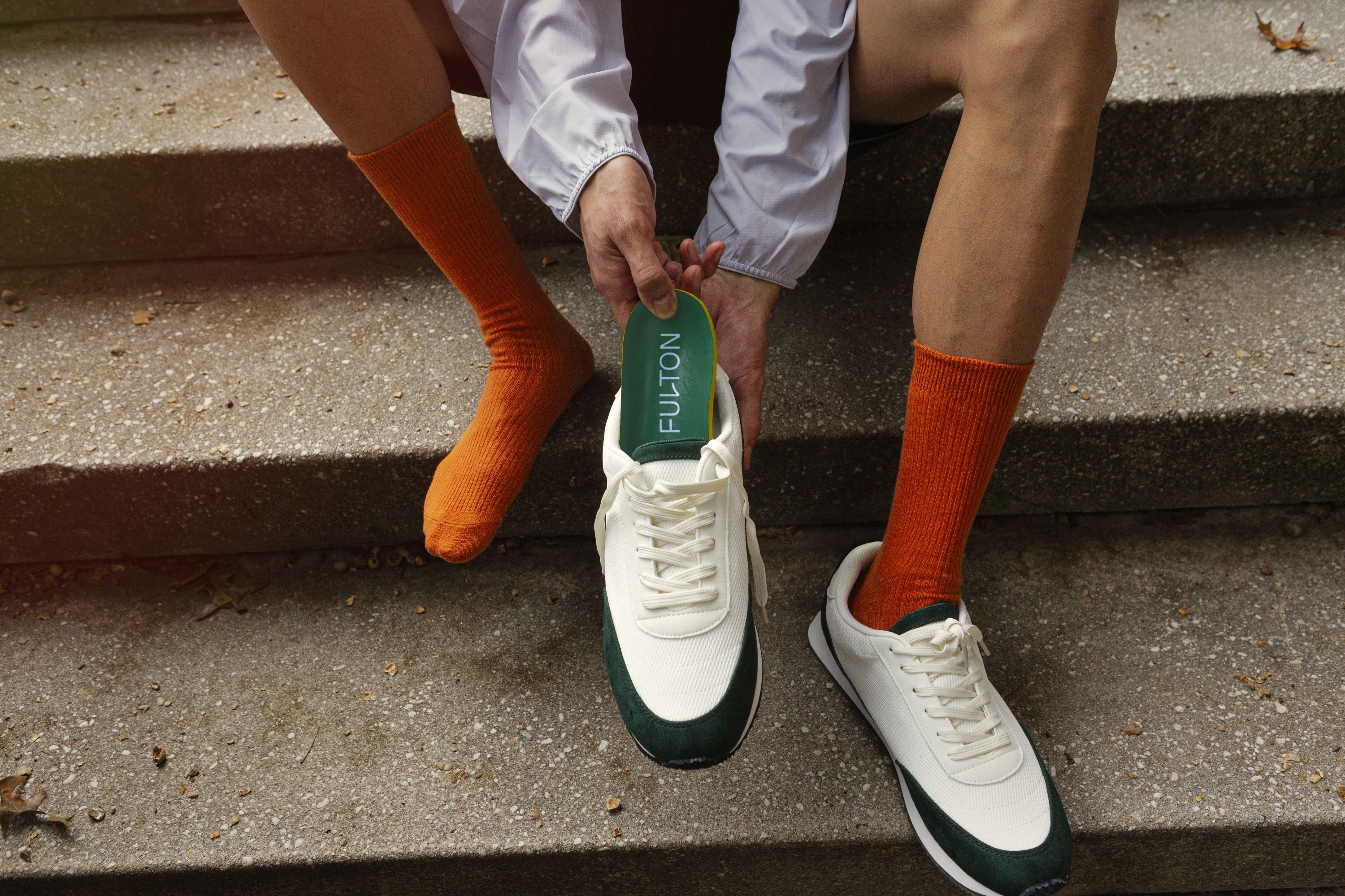 A person in orange socks putting Fulton insoles into their athletic shoes.